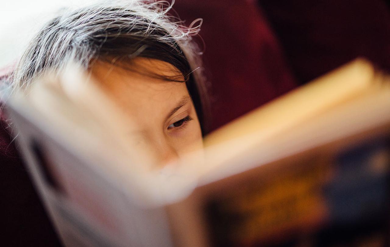 A close up of face, showing an eye, mostly obscured by a closely-held open book.