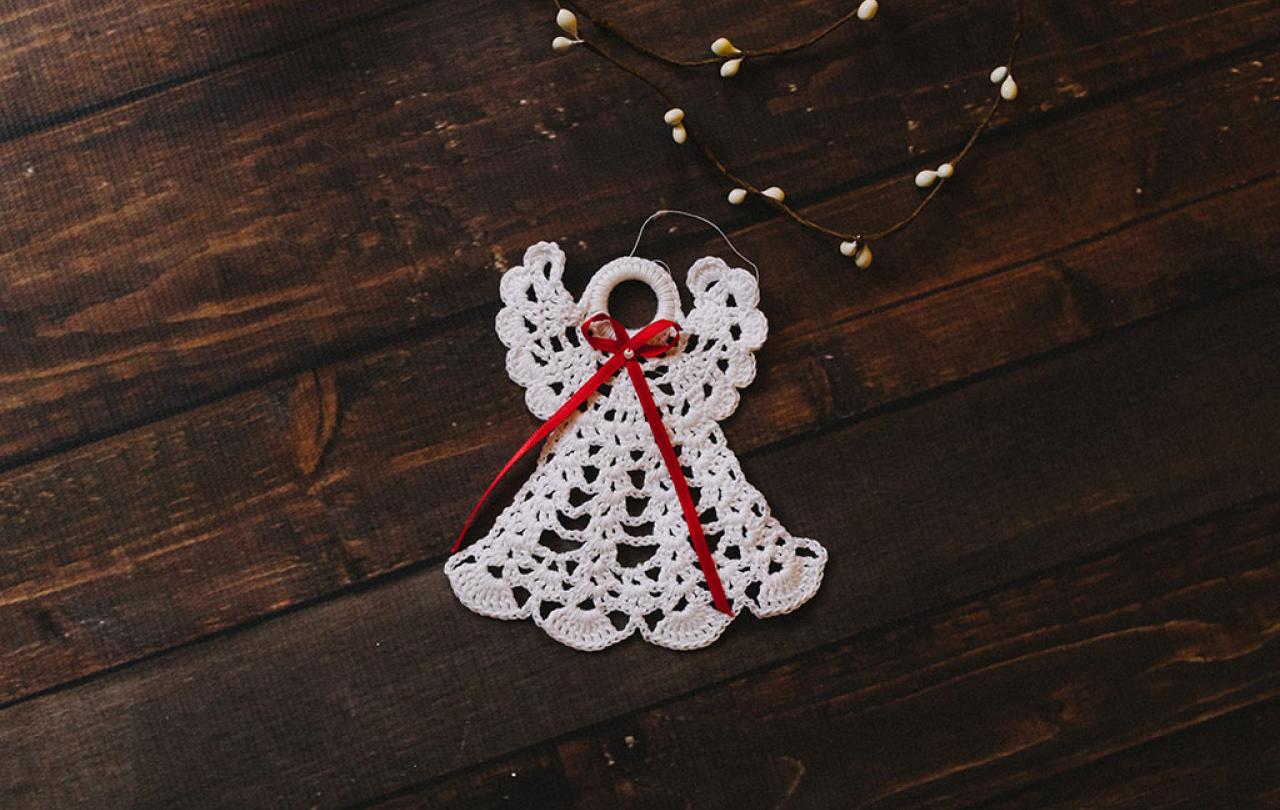 A white crocheted angel decoration against a dark background.