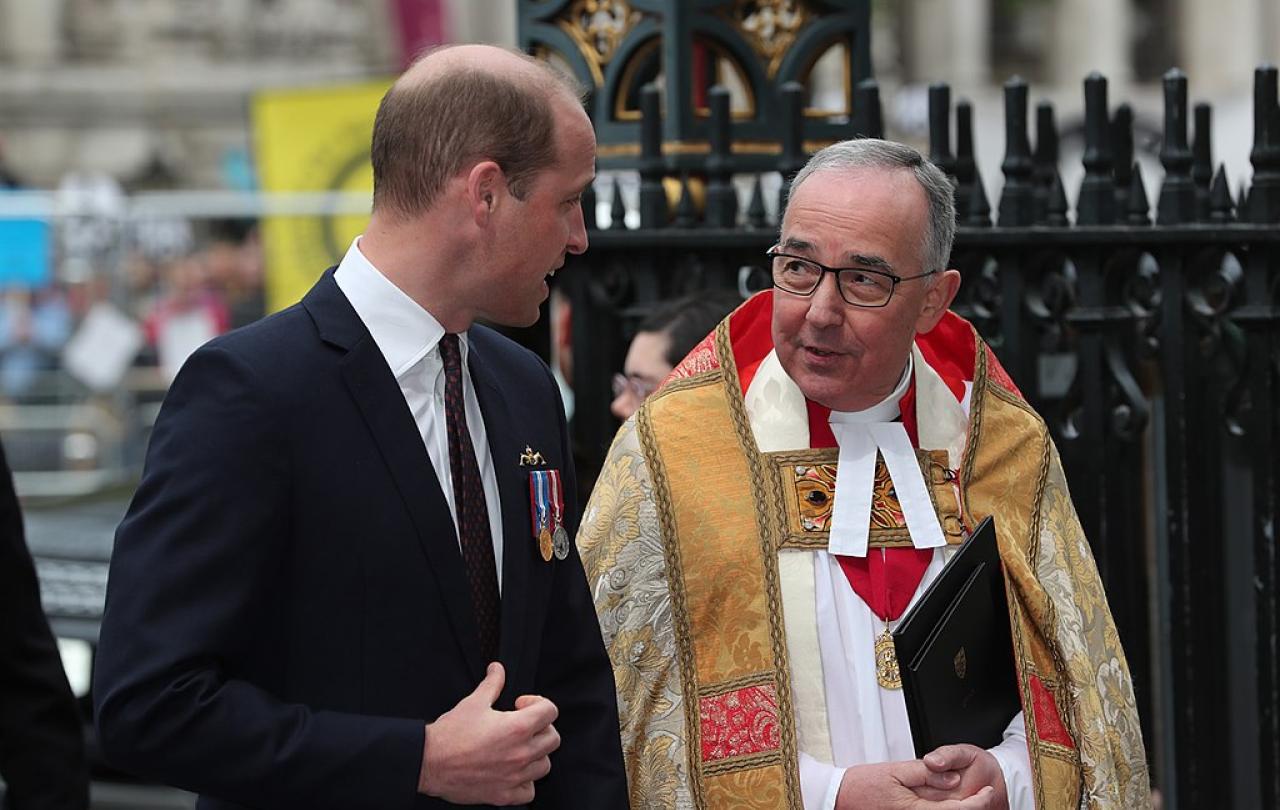 A young man wearing a dark suit talks to a minister wearing regalia.