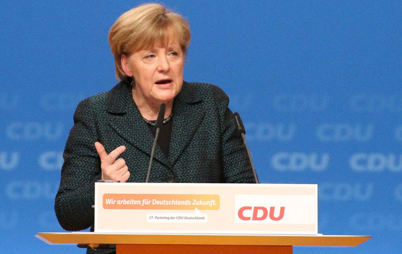 A politician stands a labelled lectern speaking and gesticulating with a hand.