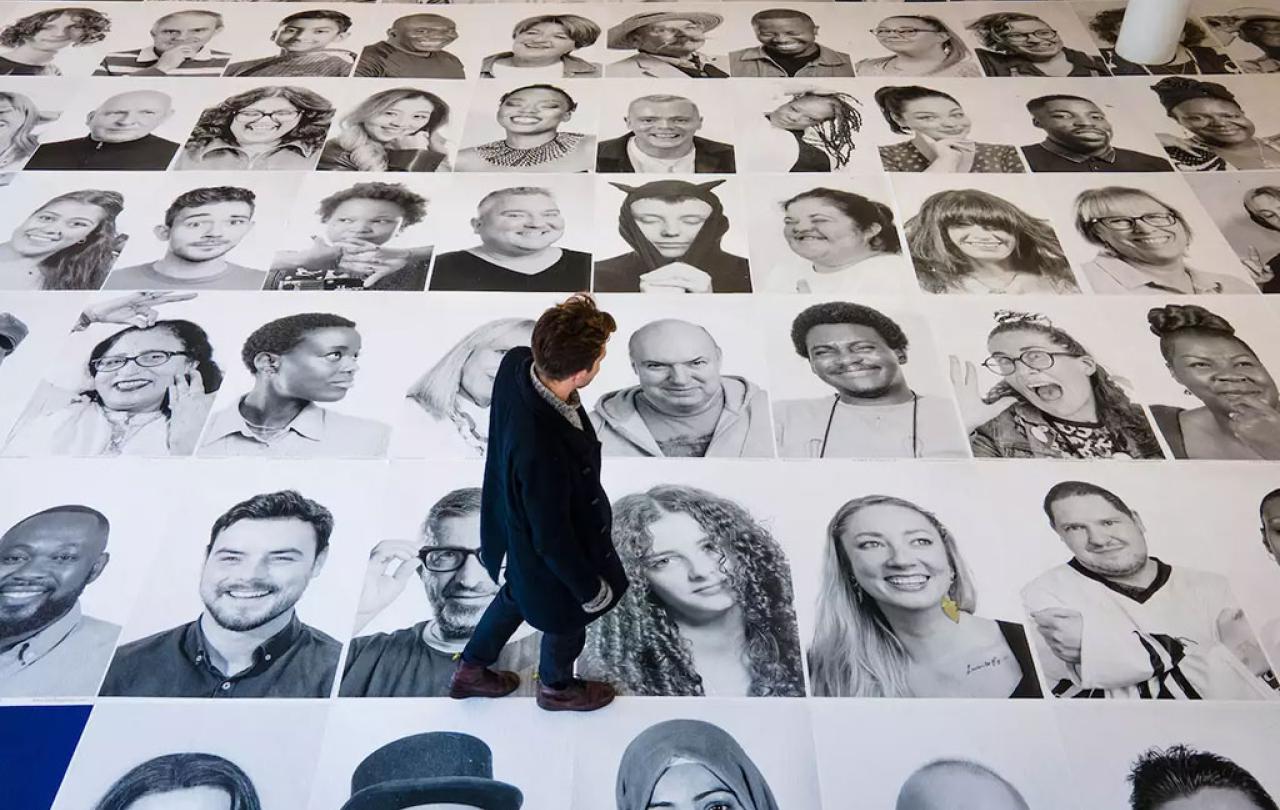 Looking down on a man walking across a grid of large black and white portrait photographs of people's faces
