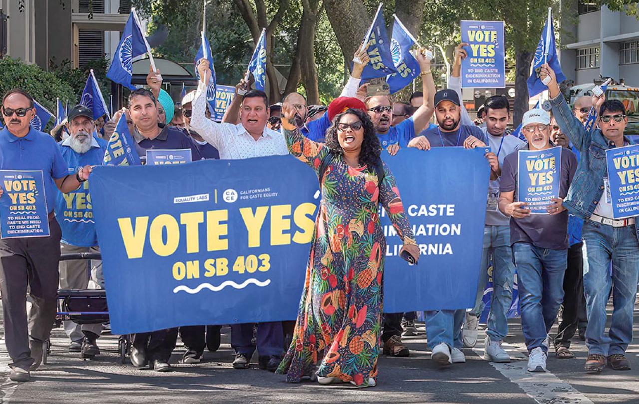 A group of protesters march behind a banner waving flags.