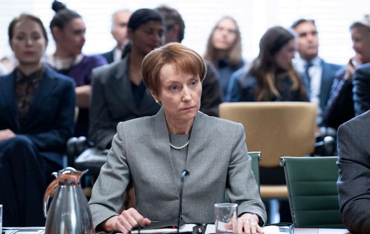 A tense-looking woman, sitting at  desk, stares into the middle disance.