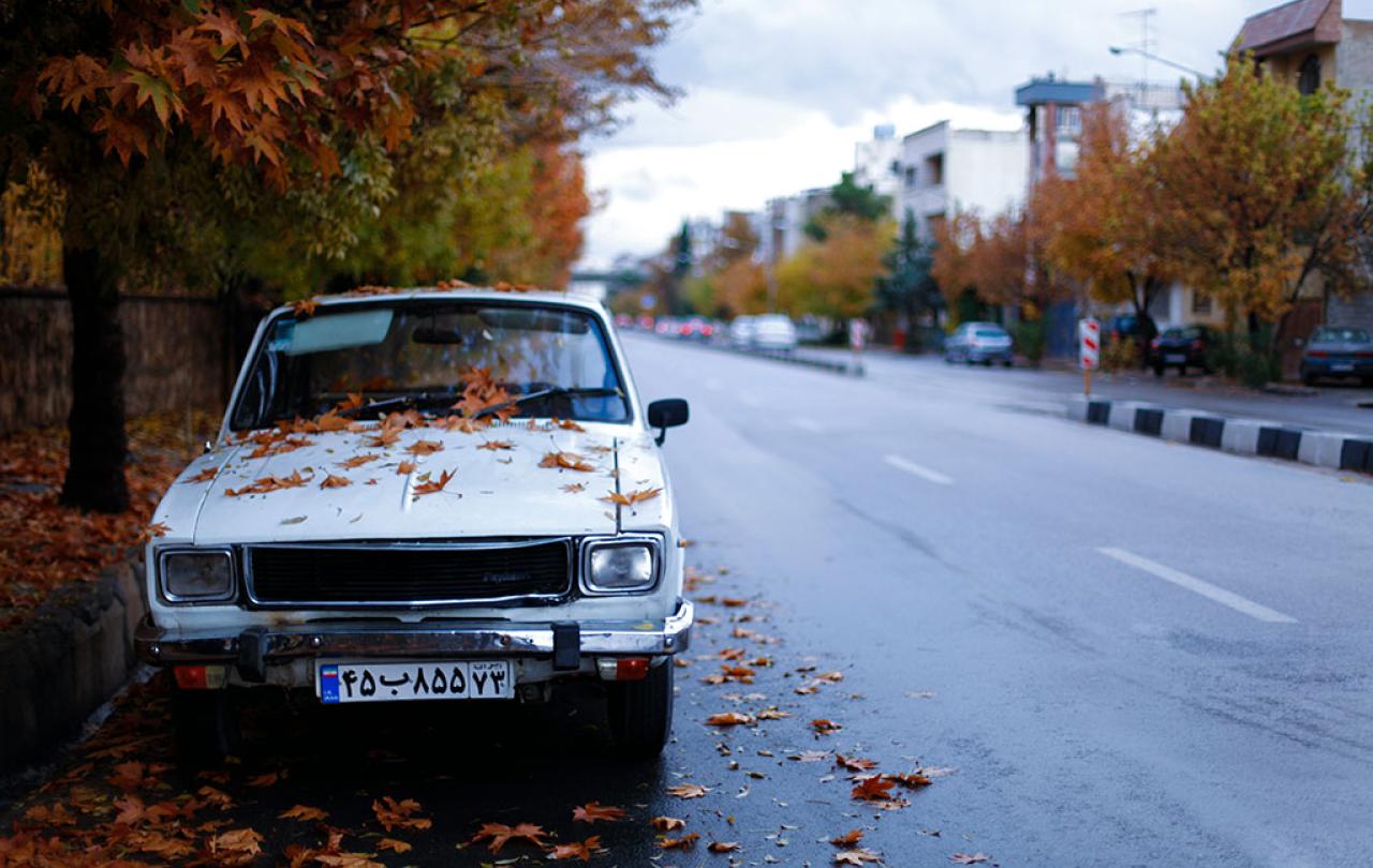 A somewat beaten white car parked on the side of a street.