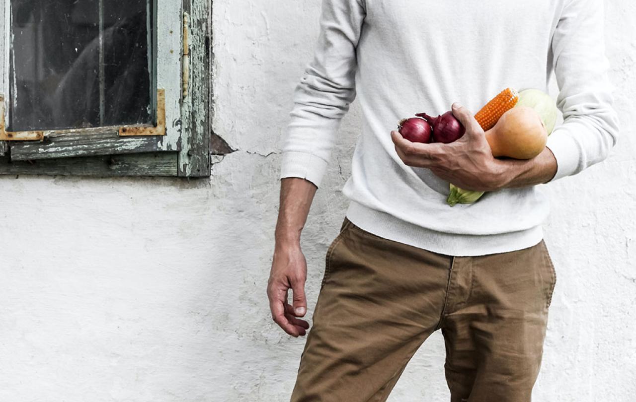 A man stands at rest, one arm holding some vegetables.