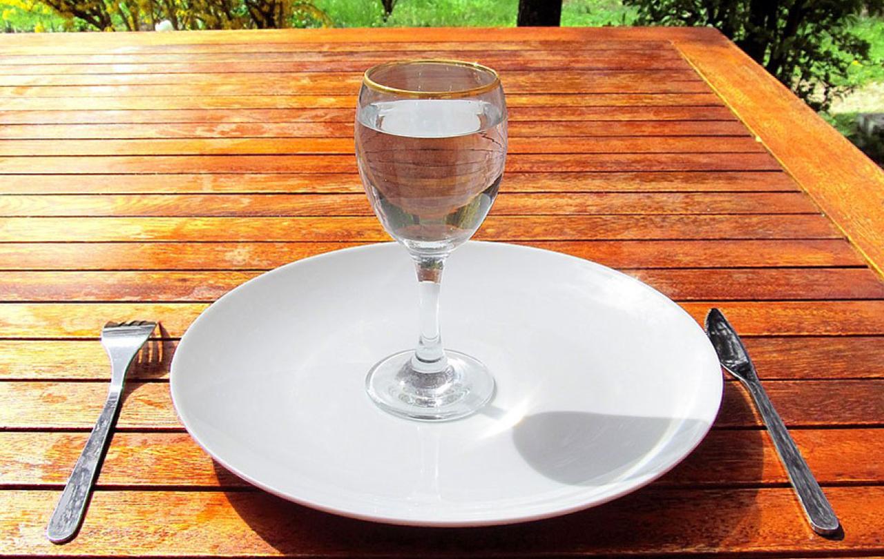 A wine glass of water sits on an empty clean plate.