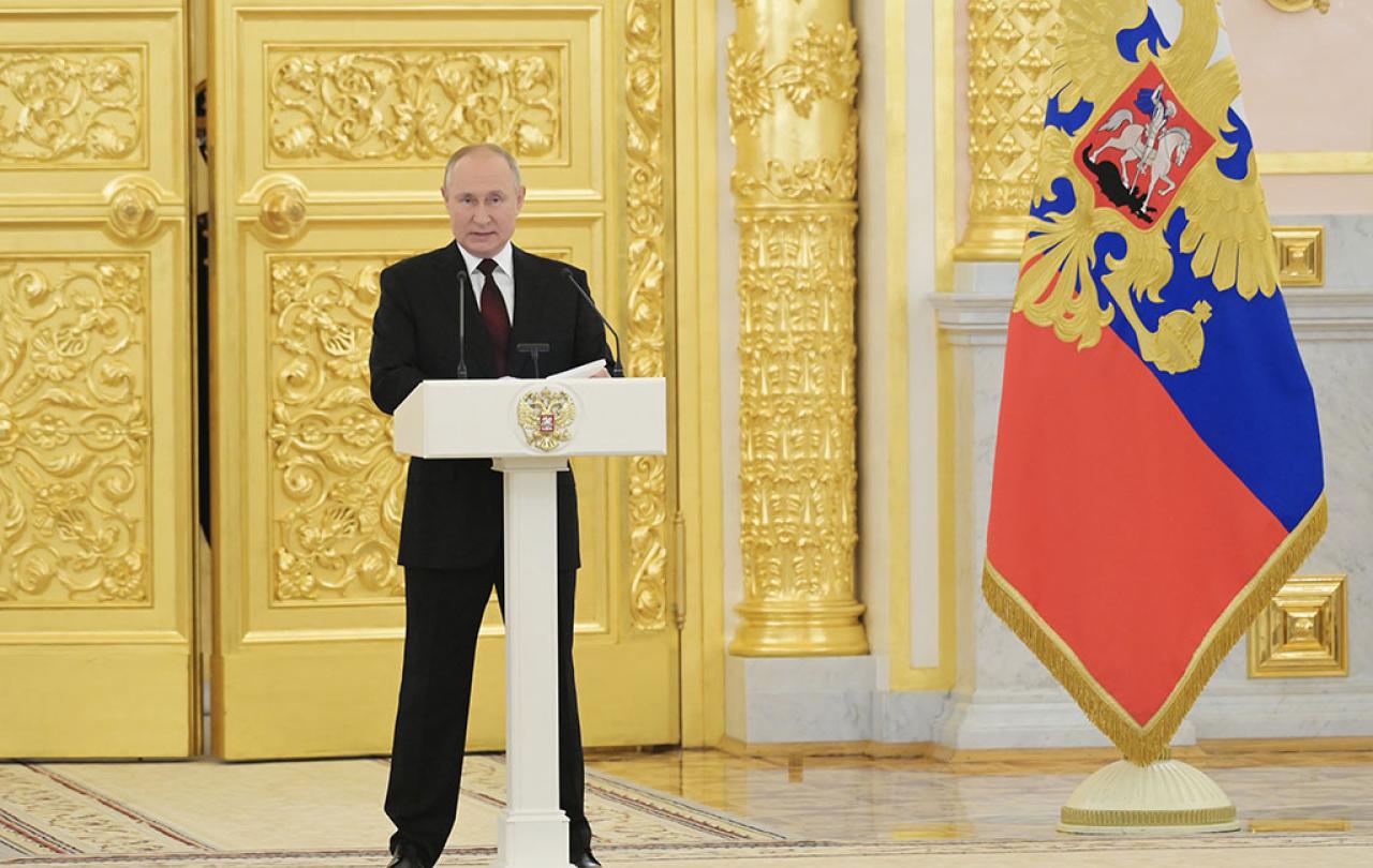 Preisdent Putin stands behind a lectern with a gold door and Russian flag behind him.