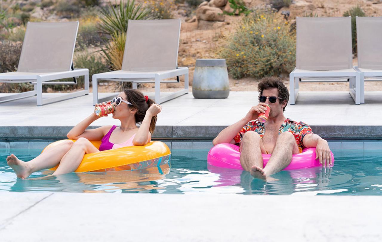 A young couple lounge on floating rings in a swimming pool.