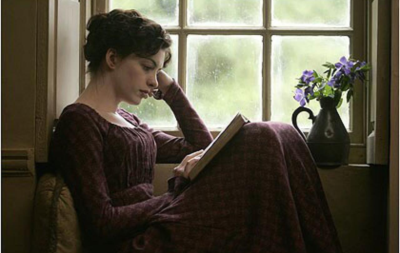 A woman in 18th century clothes sits within a windowsill reading a book