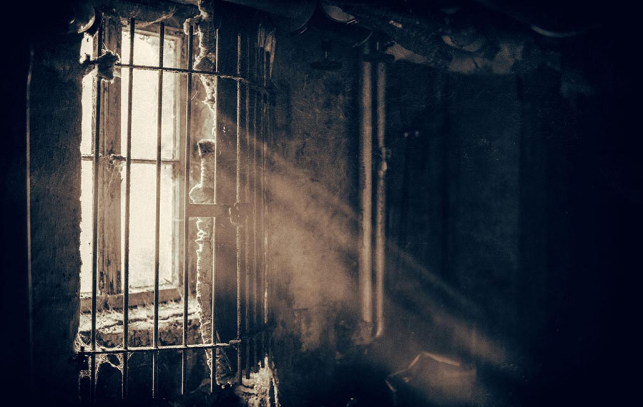 A window sheds light through locked bars into a dusty and dark room,
