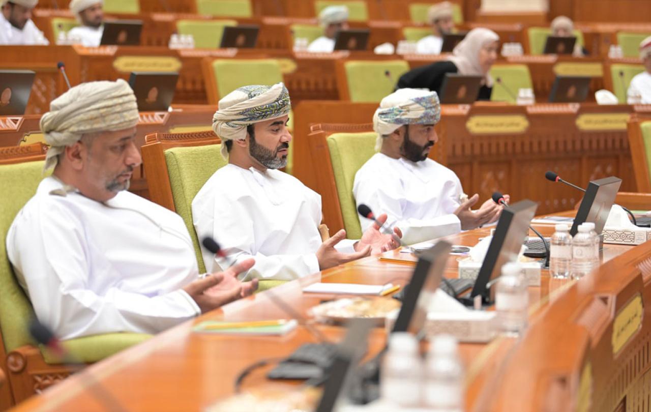 Three members of the Oman Shura sit in it's chamber and hold their hands in prayer