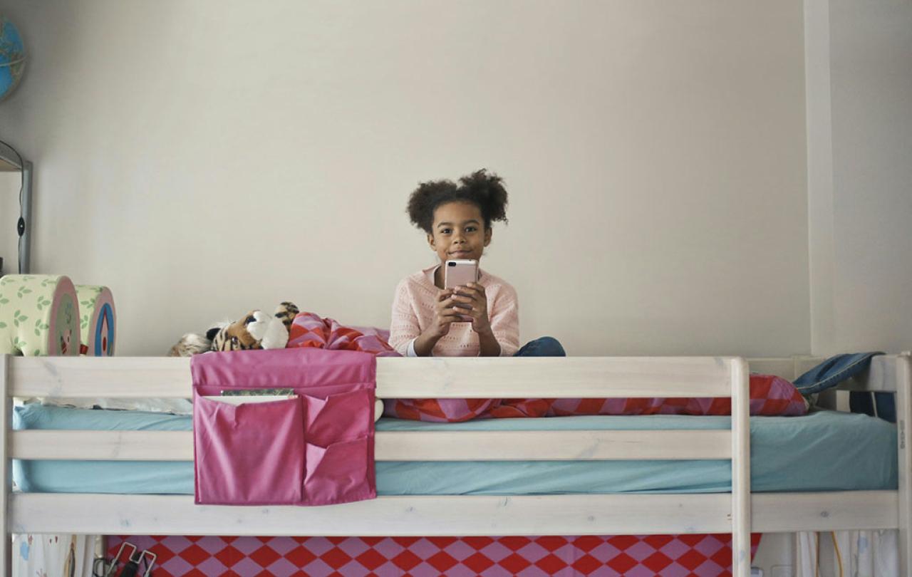 A child sits atop a bunk bed holding a phone in front.