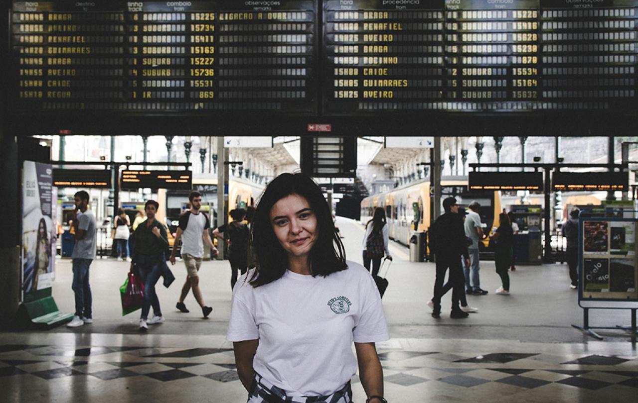 A young person stands in front of railway station platfrorms and below a large informaton display.