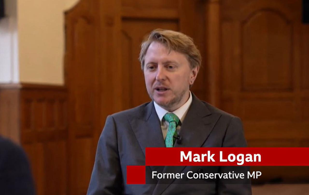 A man sits in a TV interview, below him is a captions stating 'Mark Lognan. Former Conservative MP