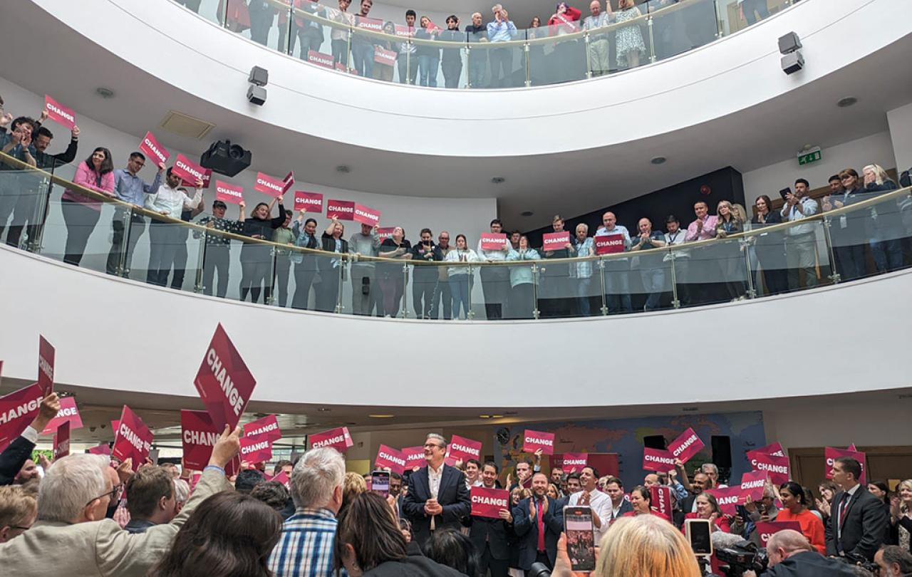 Looked down upon by crowds in galleries, a politician stands amid a throng of supporters