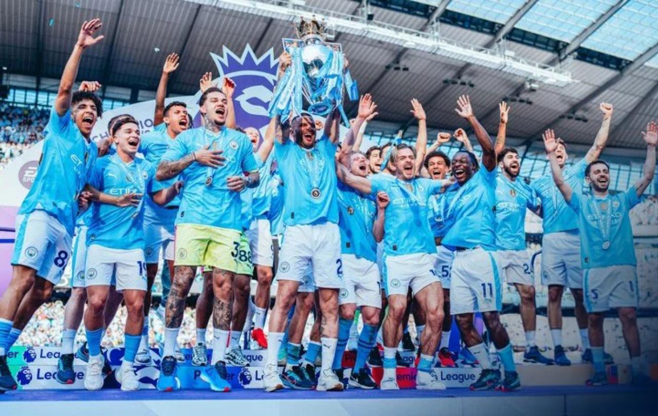 A football team wearing a sky blue kit leaps for joy holding a trophy.