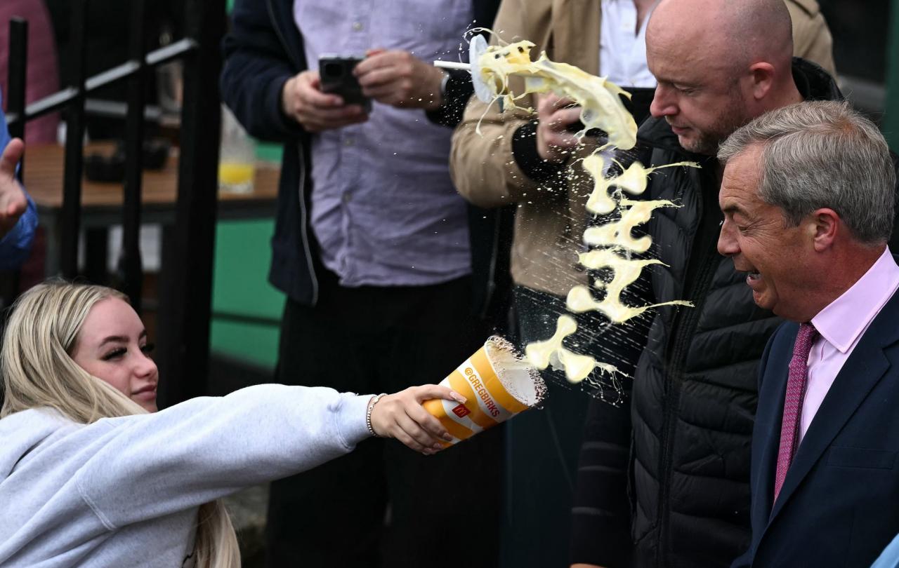 A woman throws a milkshake at a politician, the milk is mid-flight in a curved shape.
