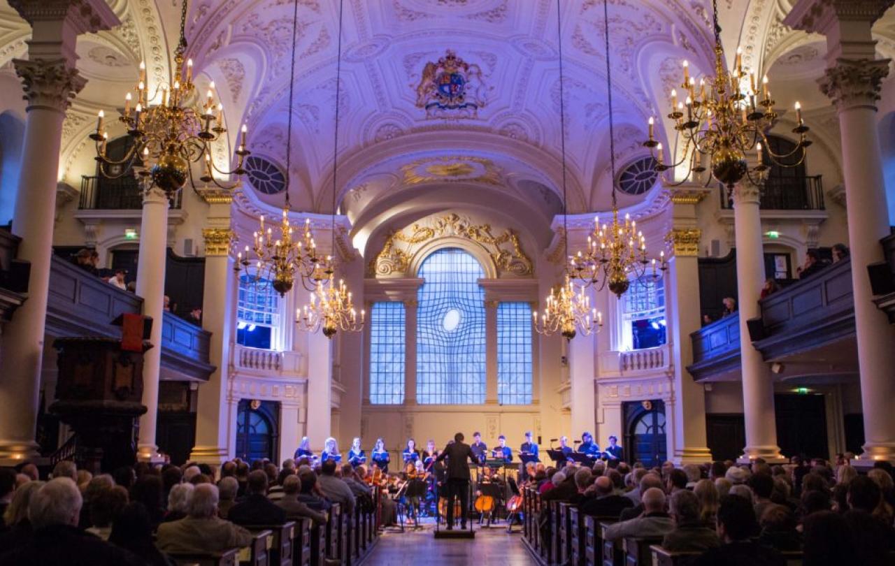 A choir sing at the front of a church while an audience looks on.