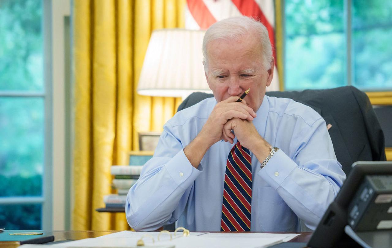 President Biden sits at a desk, holding his balled hands to his mouth.