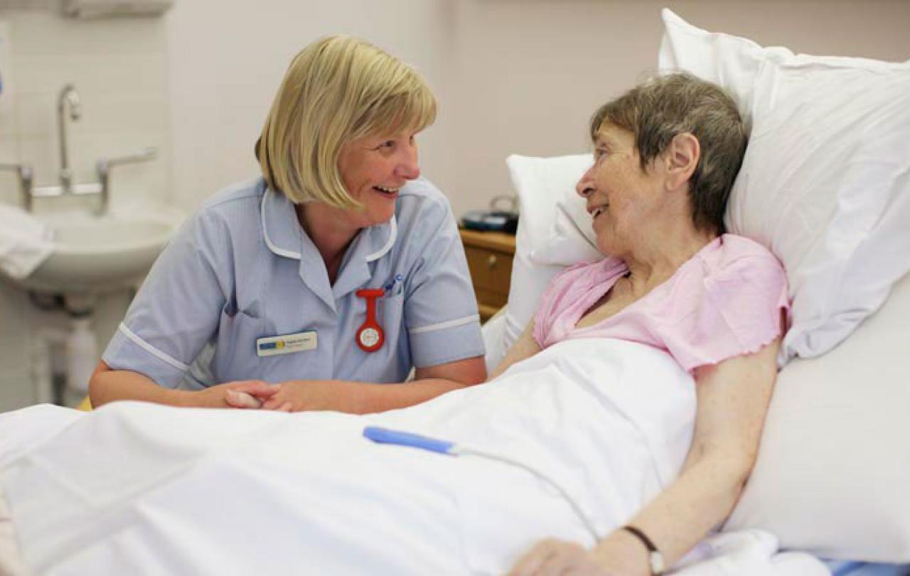 A nurse bends beside a bed and talks to a patient
