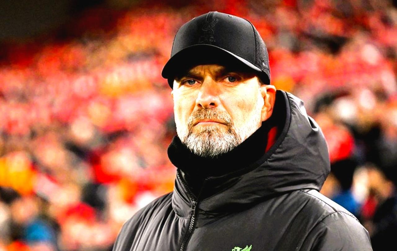 A stern looking football manager stares hard, with a stand of supporters behind him.