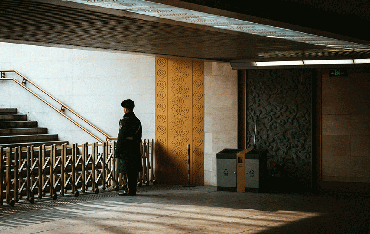 A guard stands behind a barrier across an entrance to a station escalator.