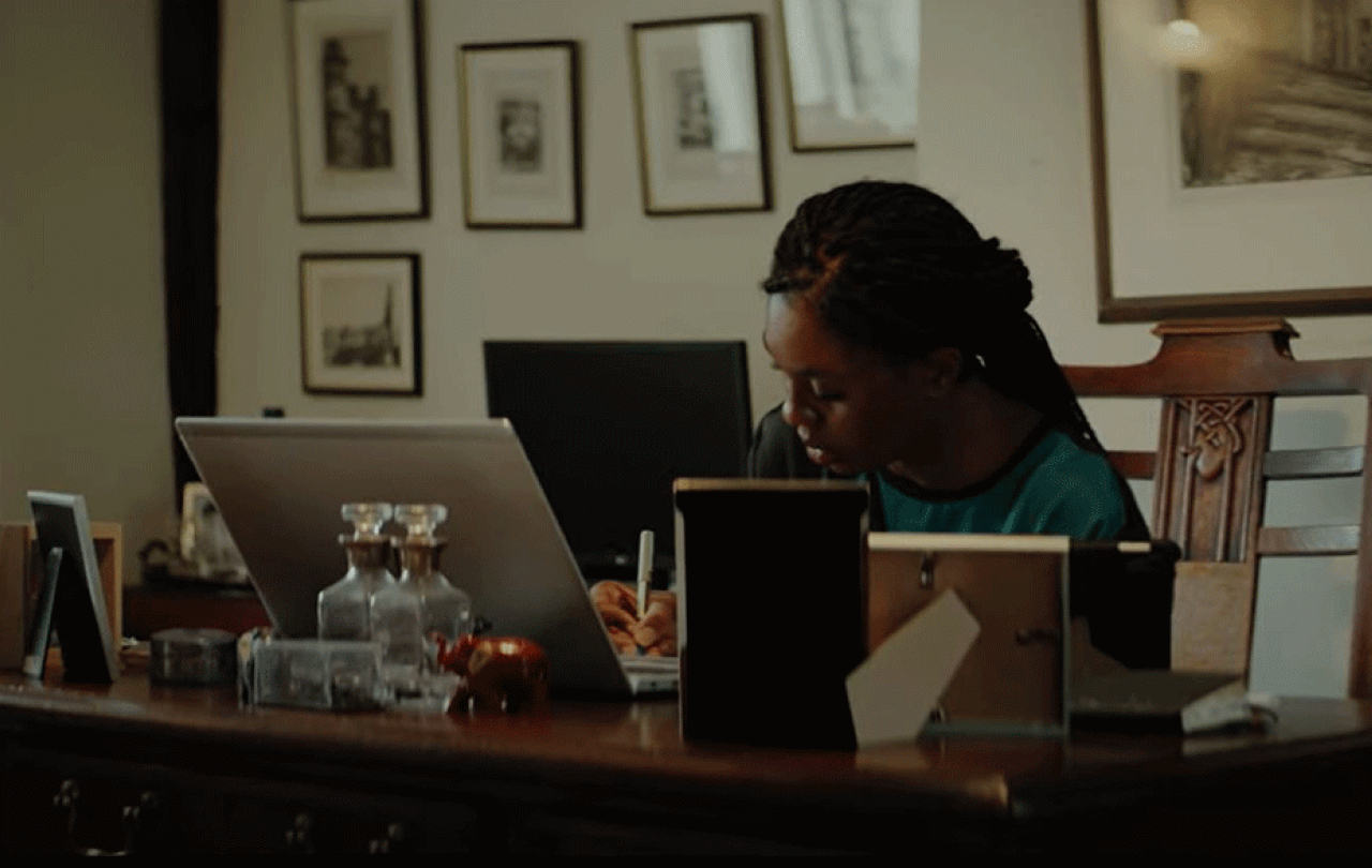 A woman works at a laptop on a desk surrounded by picture frame.