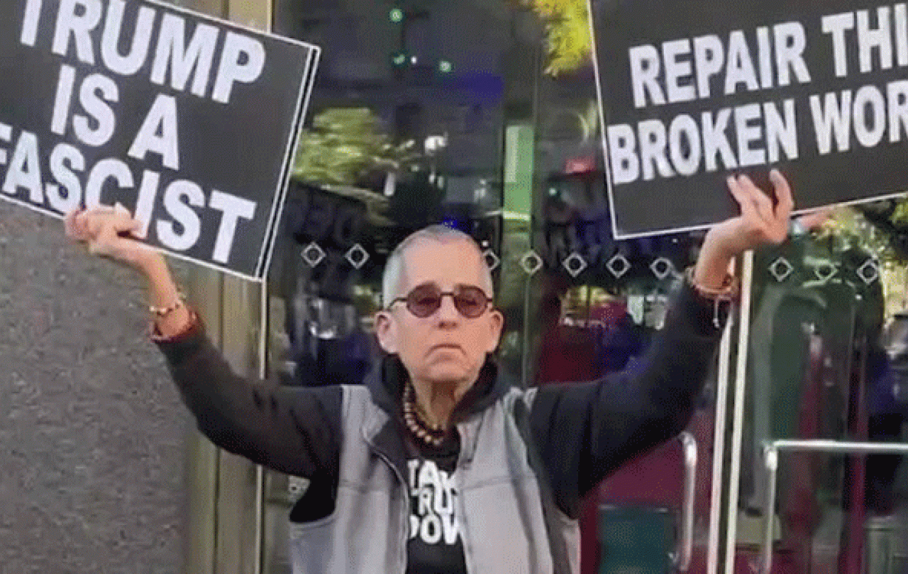 A protester holds placards up in both hands. One reads: Trump is a fascist. The other: Repair the broken world 