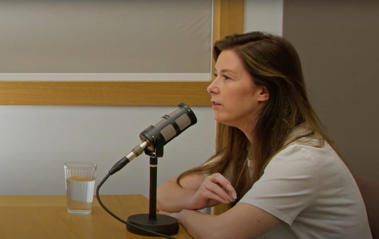 A woman leans on a table, talking into a microphone.