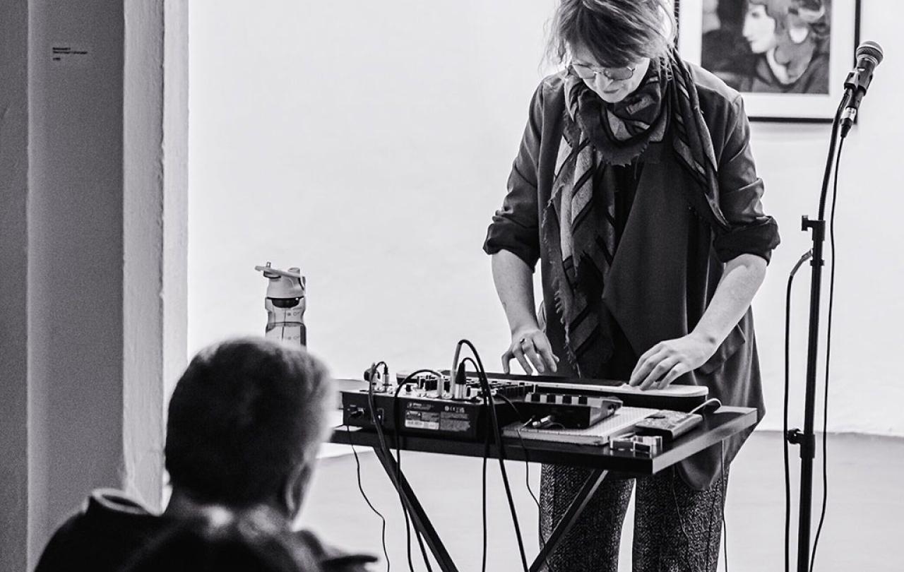 A woman stand at a mixing desk playing a small keyboard.