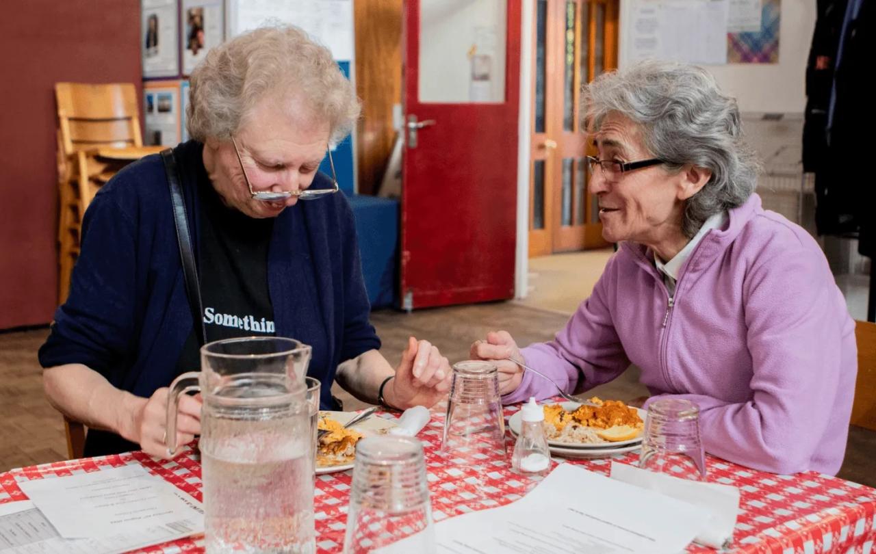 two women sit a table chatting.