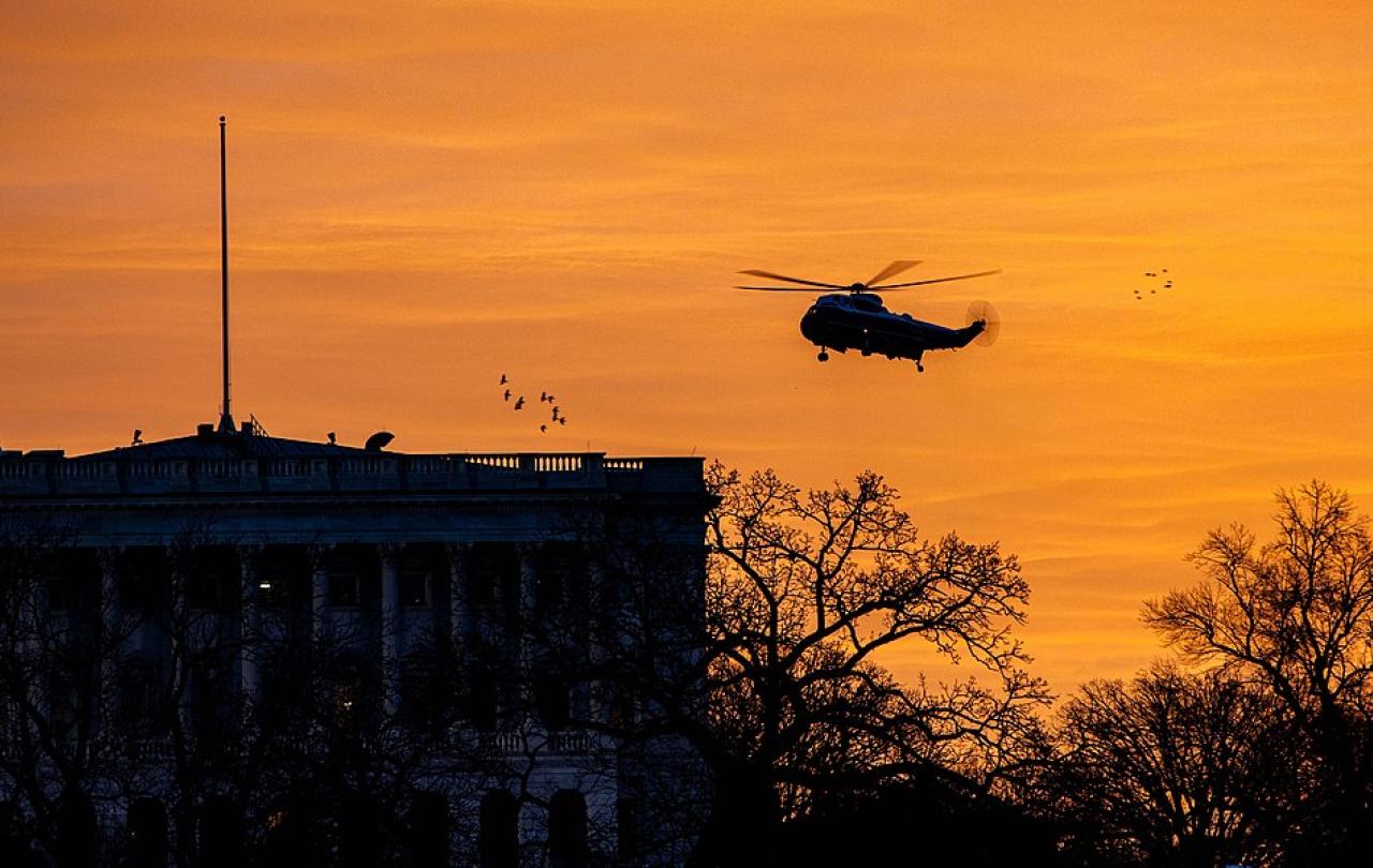 Silhoutted by a sun rise, a helicopter flies over The White House