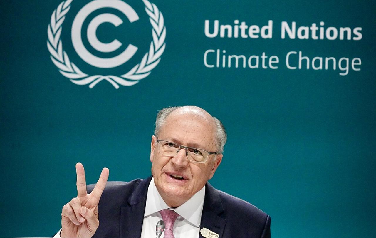 A speaker holds two fingers up while sitting in front of a backdrop reading 'United Nations Climate Change.