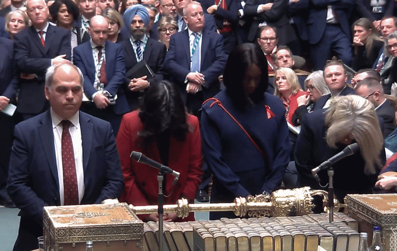 Four MPs stand at a table with heads bowed.