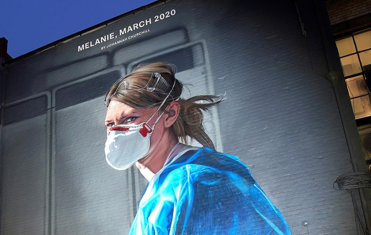 A gable end mural depicts a nurse in scrubs and a mask turning and looking towards the viewer.