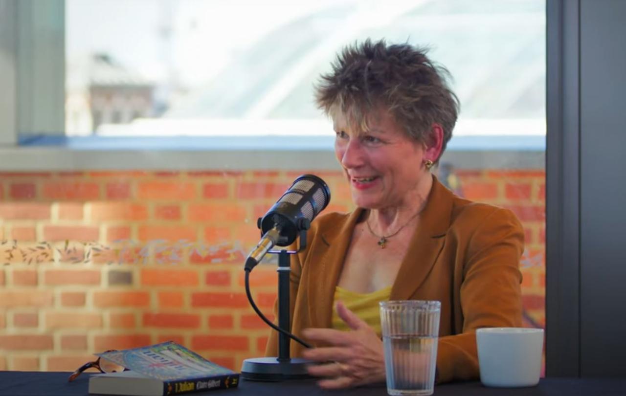 A woman sitting at a table in front of a microphone talks and gestures