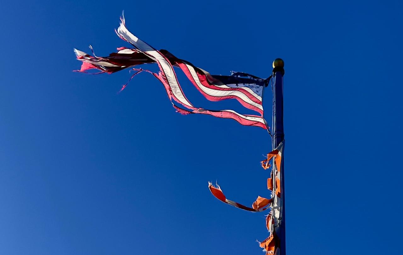 a tattered American flag flies against a blue sky.