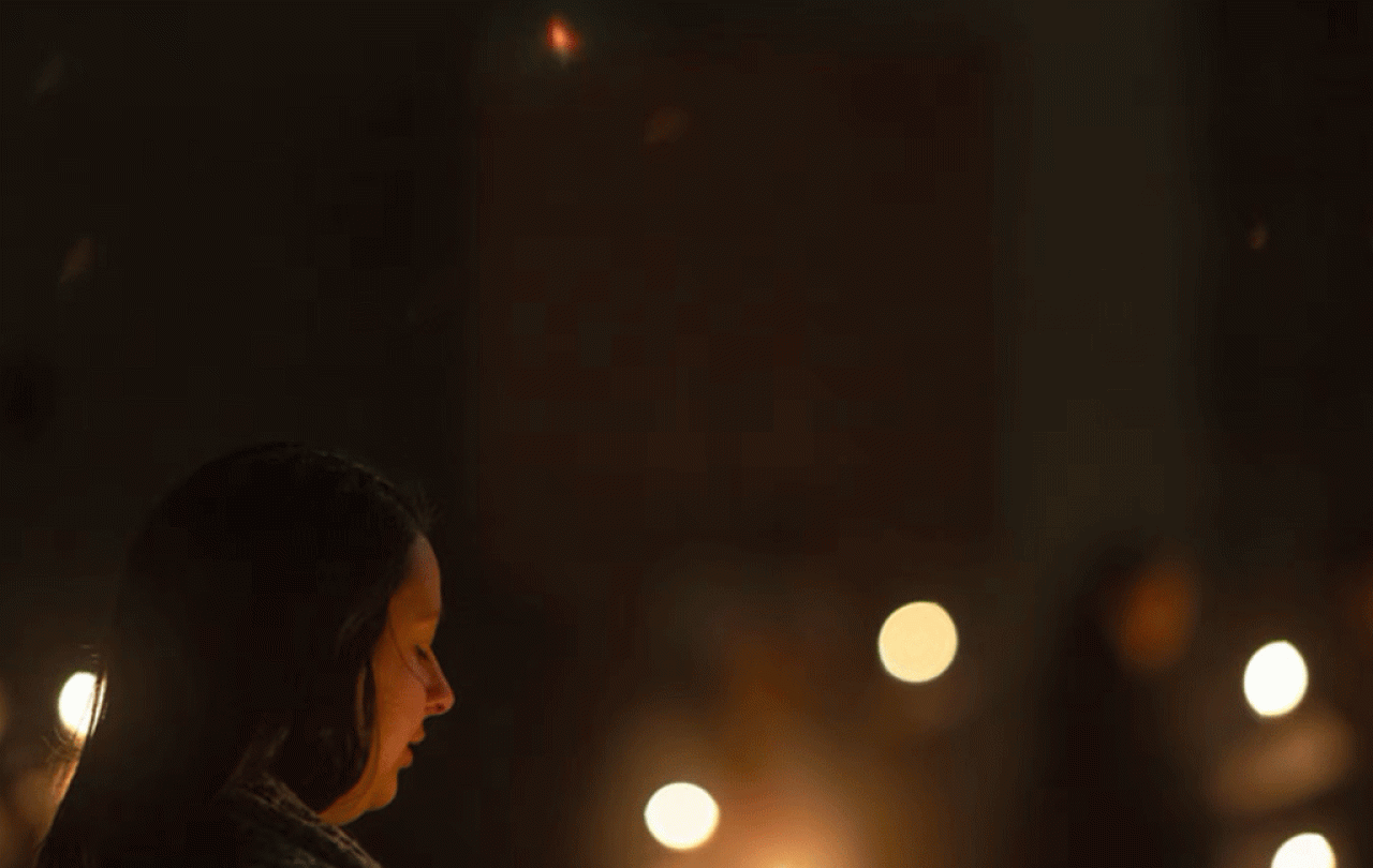 A carol singer looks down while candles flicker.