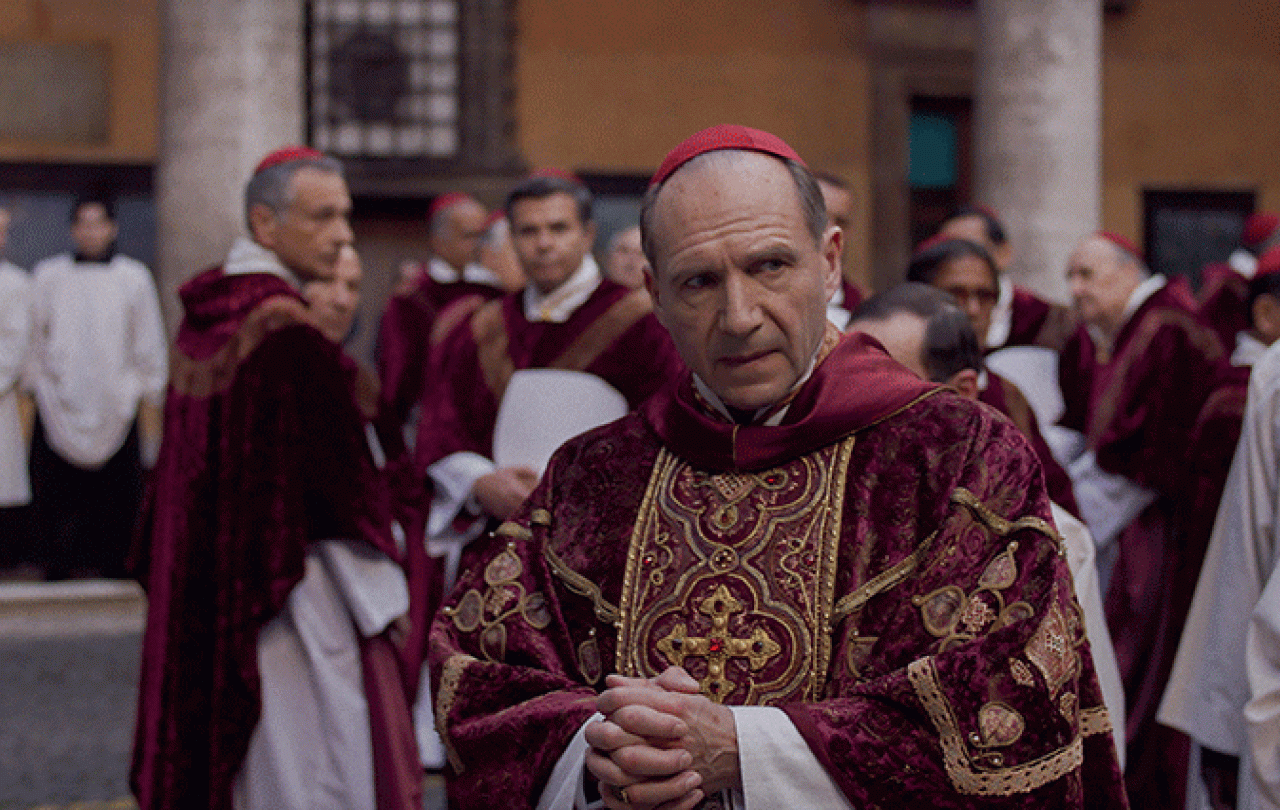 A cardinal glances to the side as he stands amid a gather of clergy,