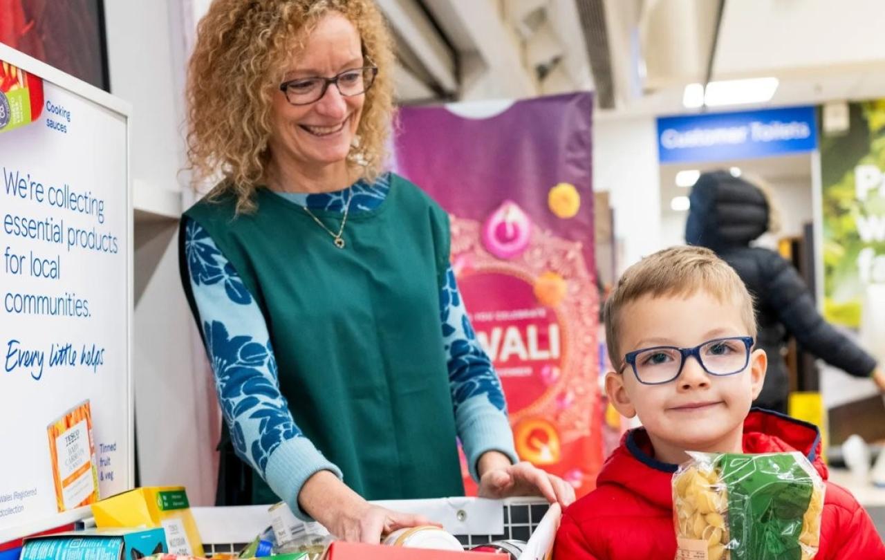 A shop assistant stands by a foobank trolley, while a child holds a packet of pasta beside it