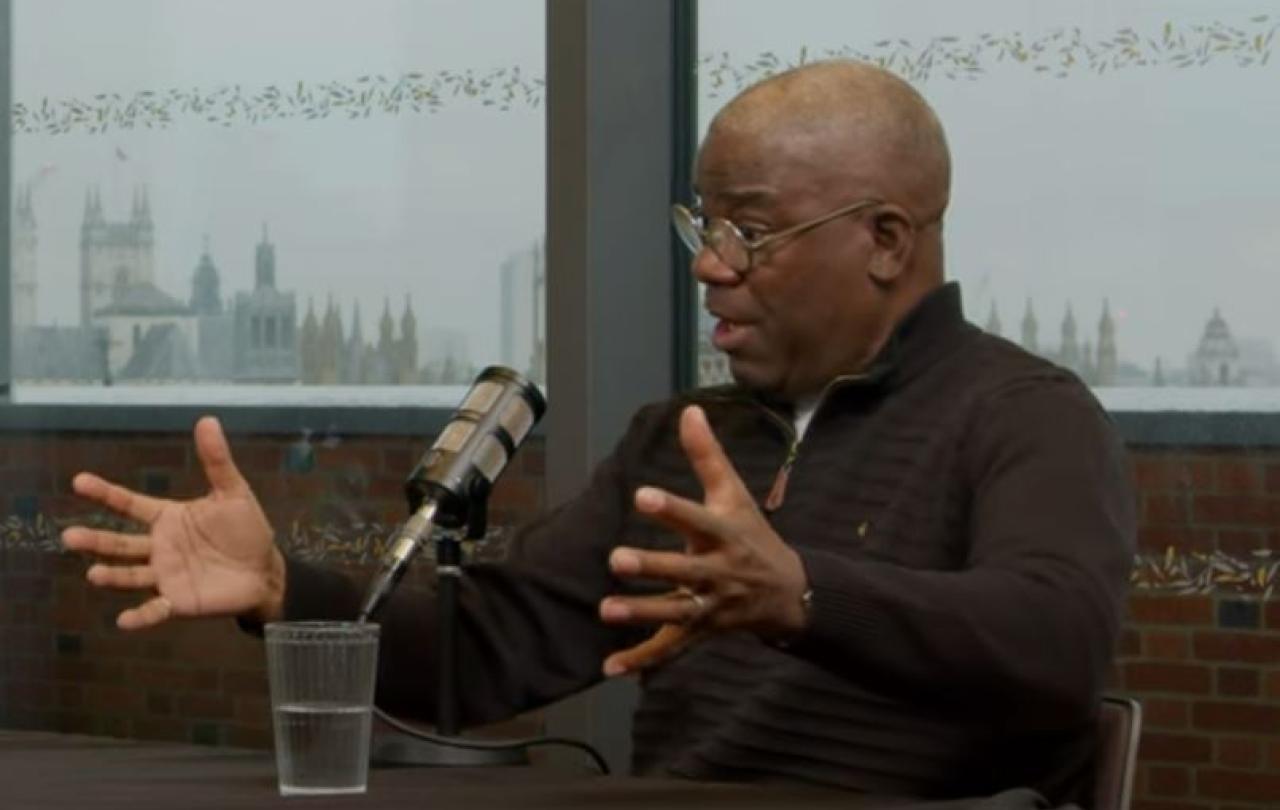 A podcast guest talks in front of a mic, while gesturing with both hands.