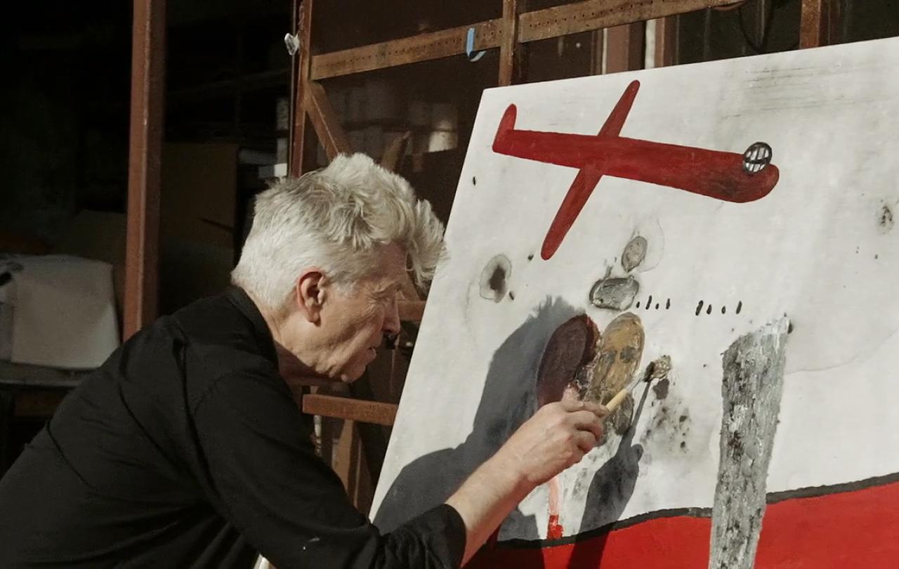A man paints a canvas with red images.