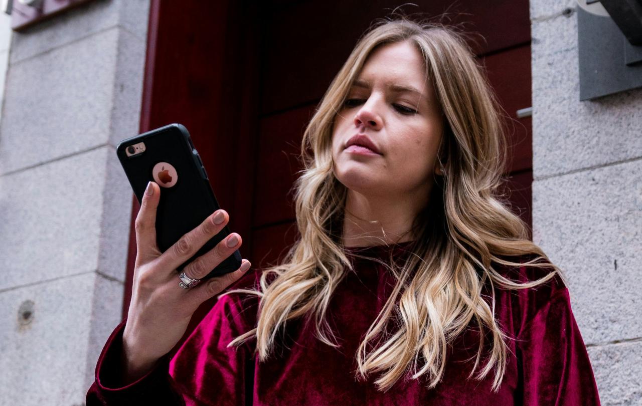 A woman holds her phone up in her hands and looks at it in a slightly vexed way.
