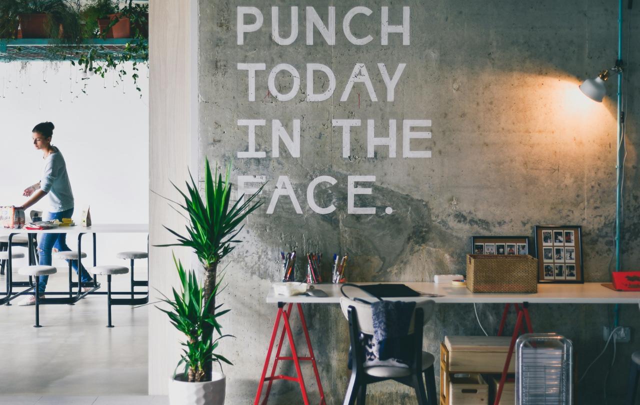 An office wall displays a huge motto reading 'punch today in the face'