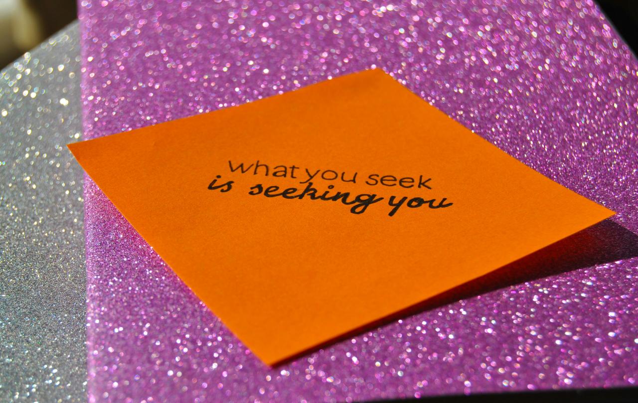 Against a purple glittery background, a orange notelet reads: 'what you seek is seeking you.'