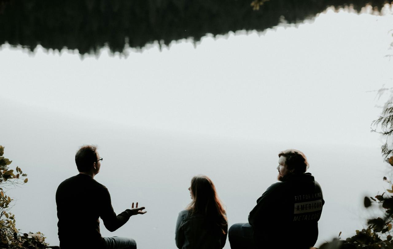 Three people sitting looking out over viewpoint are silhouetted against the sky. 