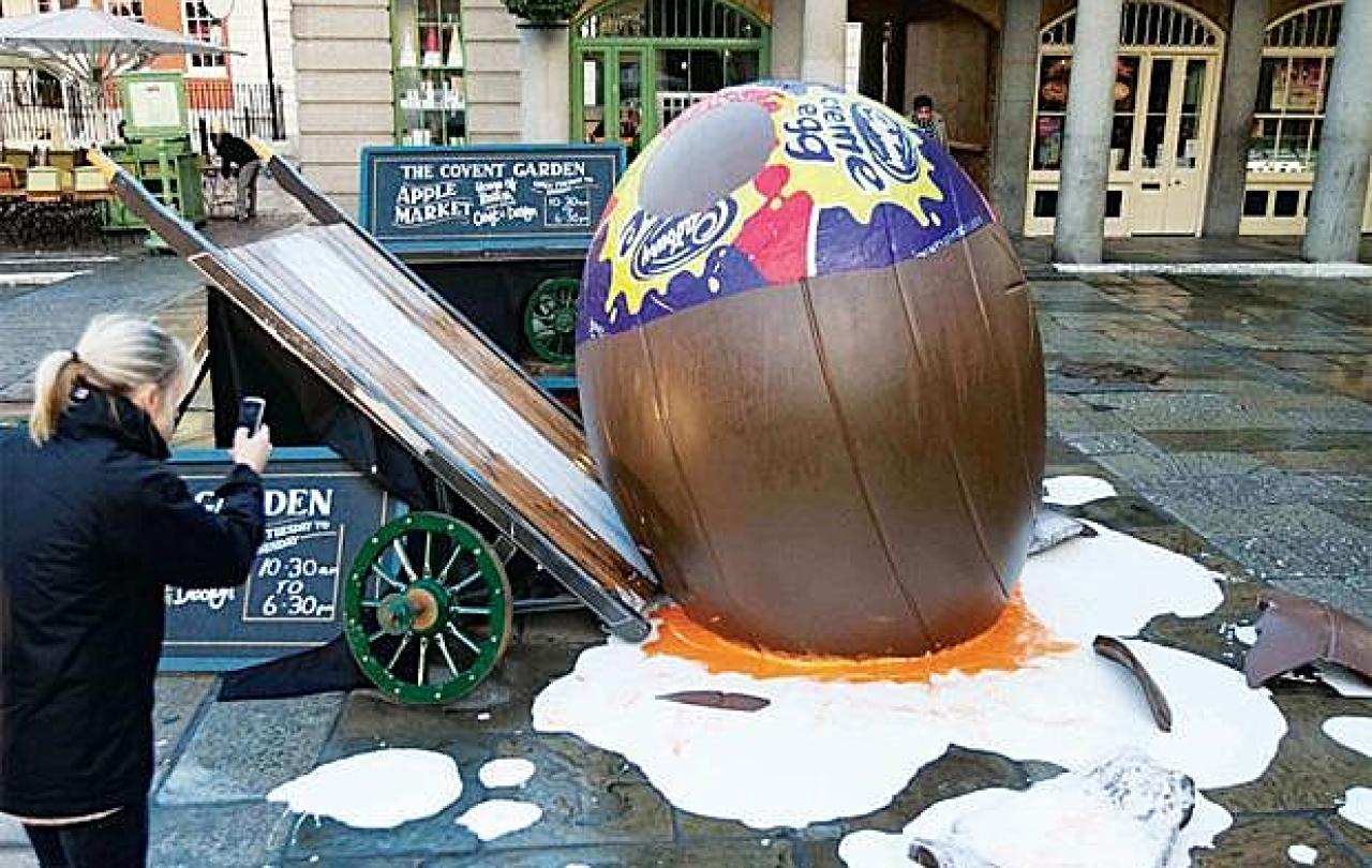 A giant creme egg lies smashed on the ground beside a tilted market barrow.