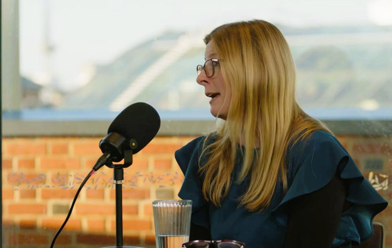 A woman sits at a table and talks with a microphone on a stand in front if her,