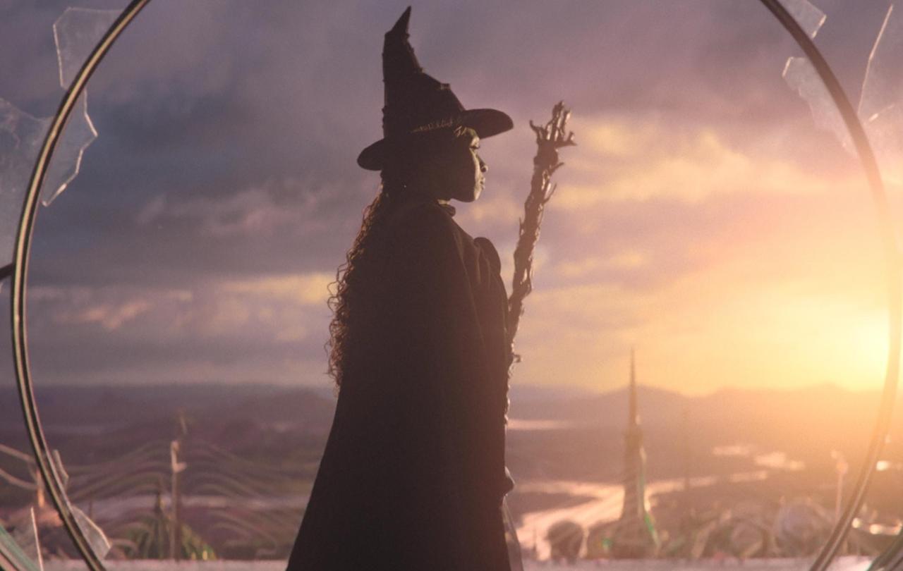 In a still from Wicked, the witch stands and looks to the sunset.