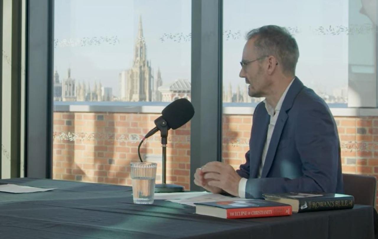 A podcast guest sits at a table in front of a mic. 